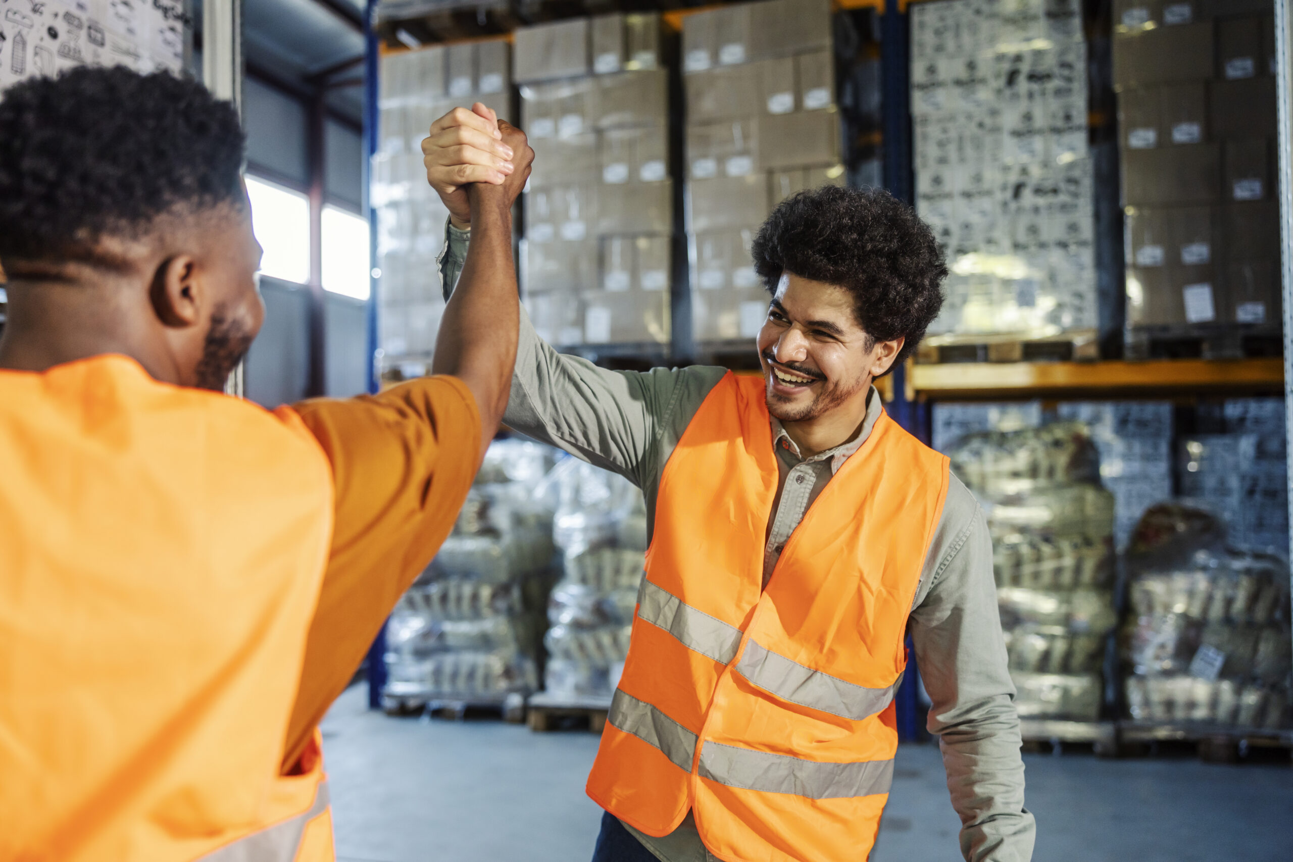 Experienced professional storage workers having bro handshake at facility. Happy team celebrating collaboration
