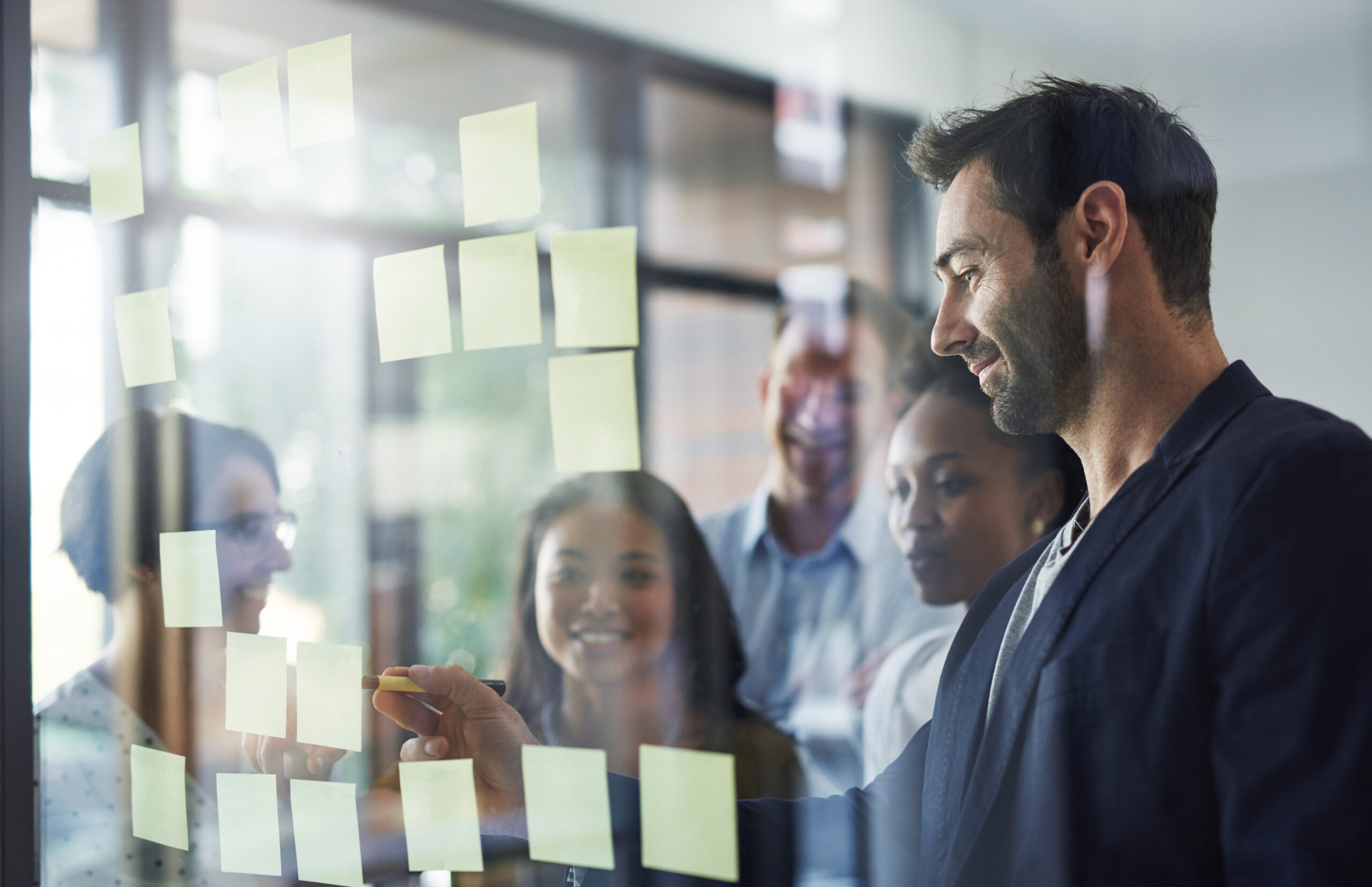 Idea, glass and business people in meeting for brainstorming, discussion and planning in office. Creative company, startup and workers writing on sticky notes for teamwork, research and project.